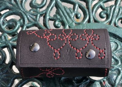 mini trousse cylindrique en cuir pleine fleur noir avec sa broderie rouge en lacet continu