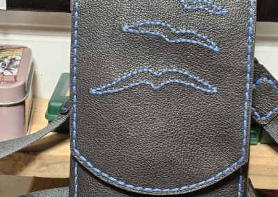 Pochette bandoulière en cuir noir grainé et souple avec broderie bleu océan représentant 4 oiseaux